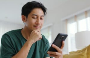 Young man sat on sofa reading on his phone