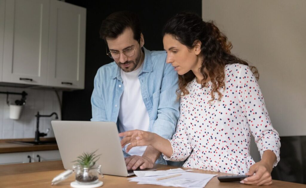 Two people reviewing information on a laptop at home in a modern kitchen.