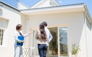 Real estate agent showing a modern house to a couple on a sunny day.