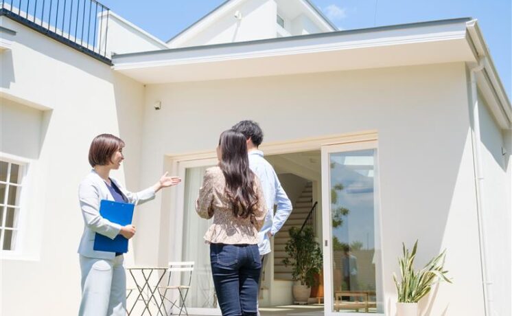 Real estate agent showing a modern house to a couple on a sunny day.