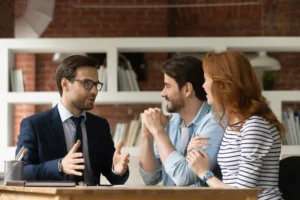 An estate agent in a suit discusses property options with a happy couple in an office.