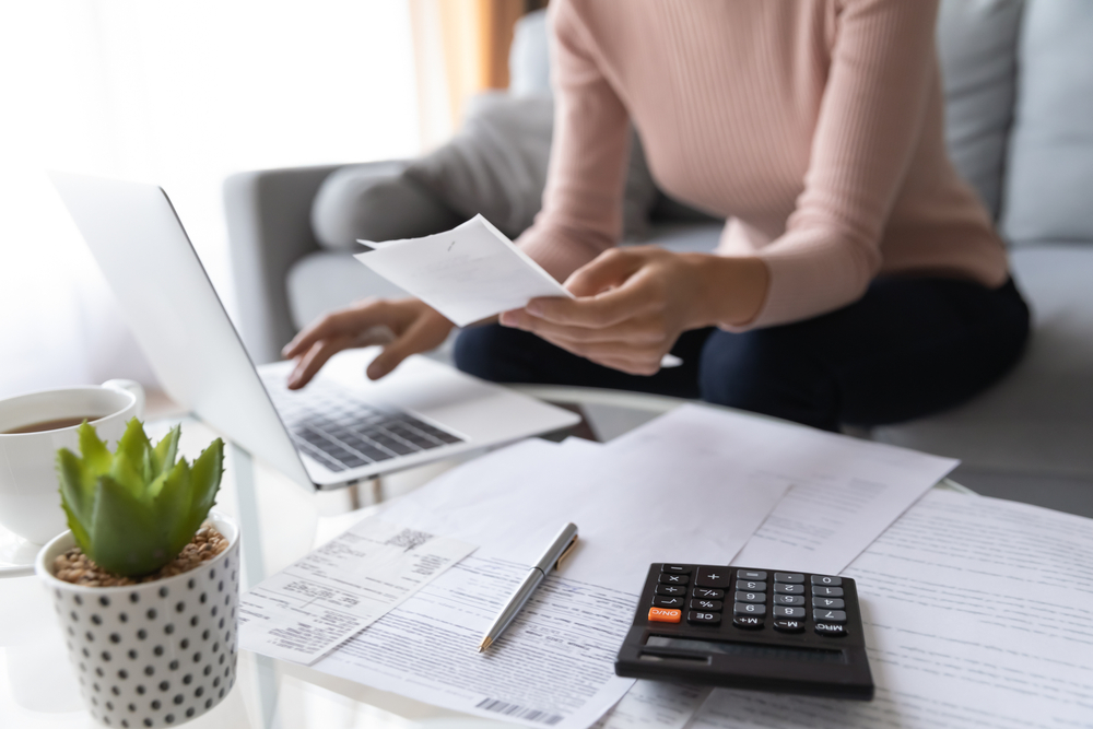 A woman managing finances with a laptop, receipts, and a calculator on a table.