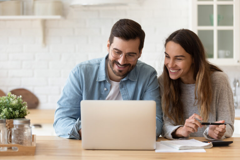 A happy couple smiling while looking at a laptop in a bright, modern kitchen.